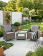 Rattan garden furniture set with two armchairs and table on modern patio surrounded by plants