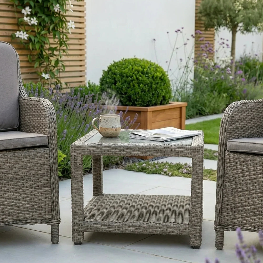 Rattan garden coffee table with glass top arranged on patio between two chairs