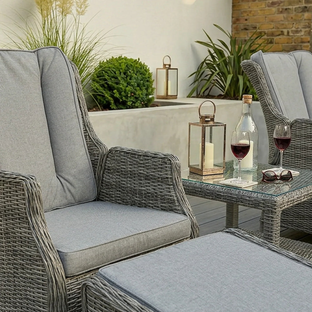 Grey rattan garden chair set with cushions, ottoman, glass table, wine glasses and lanterns
