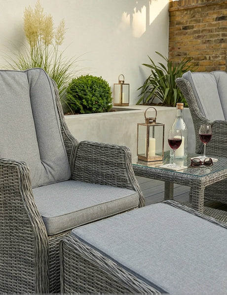 Grey rattan garden chair set with cushions, ottoman, glass table, wine glasses and lanterns