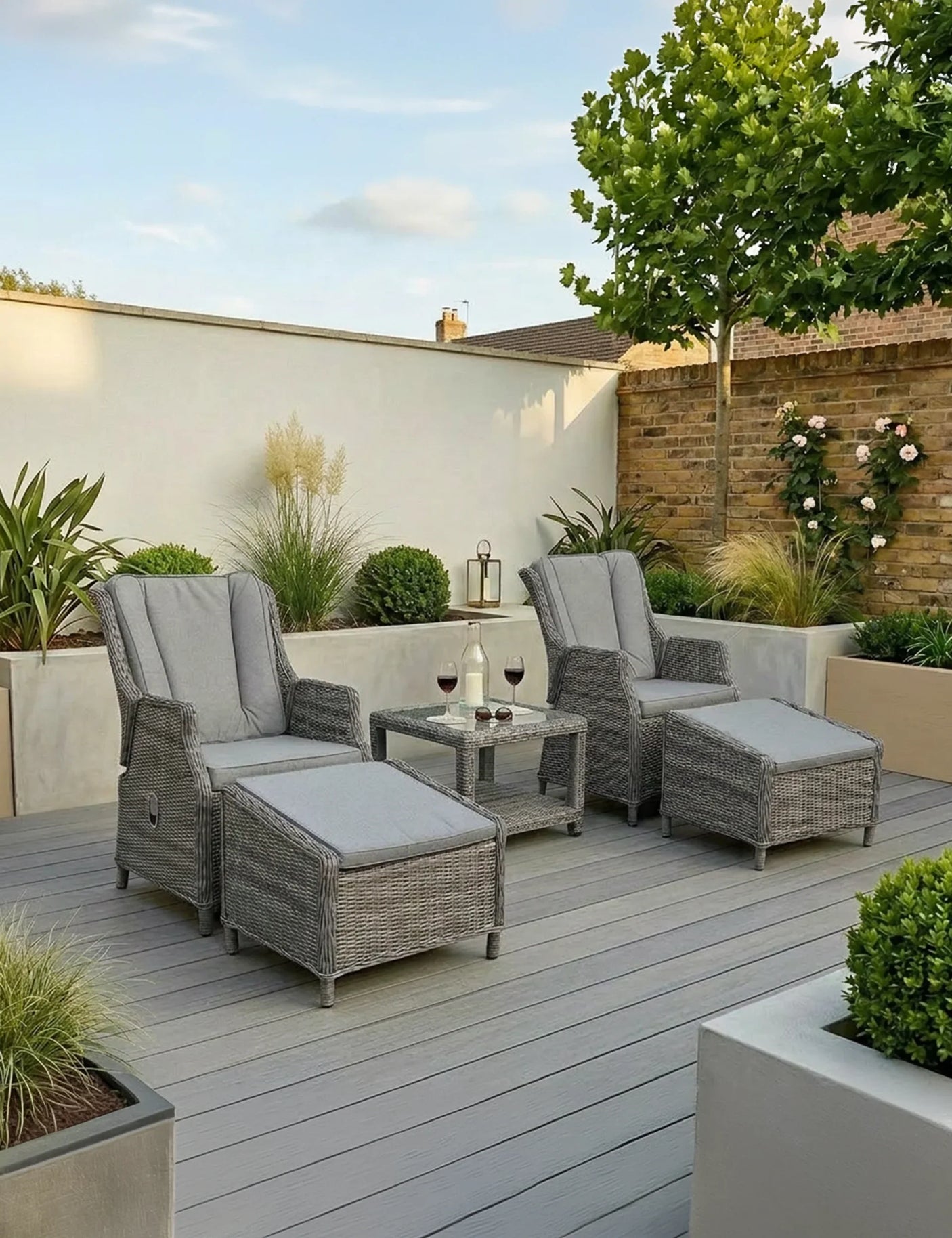 Grey rattan reclining garden chairs with cushions and matching footstools on modern patio