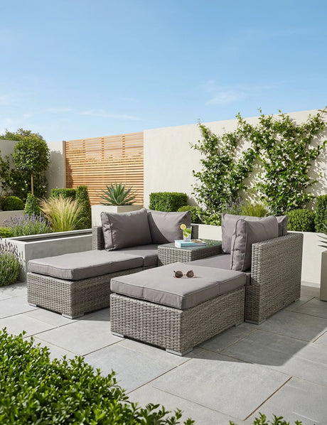 Grey rattan outdoor sofa set with cushions and glass-top table on a modern patio
