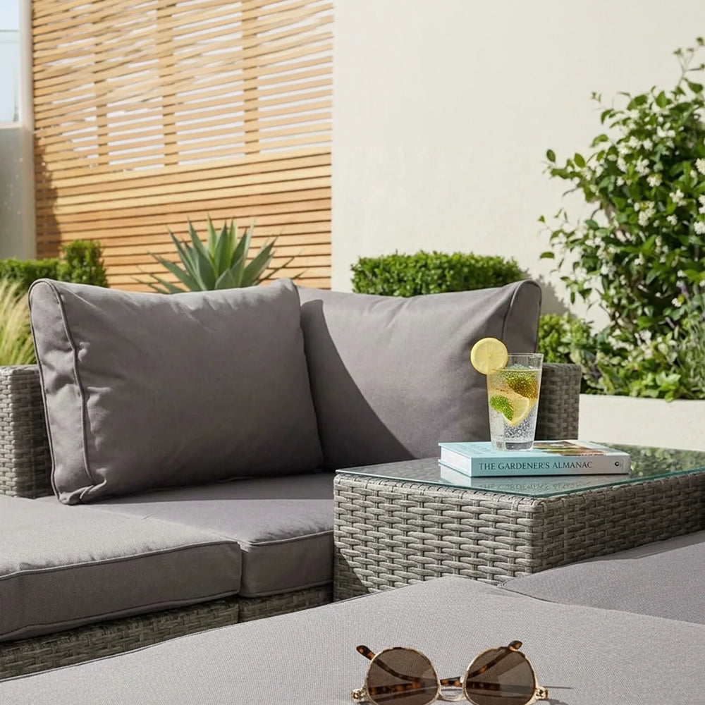 Grey rattan garden sofa set with cushions, side table, sunglasses, and glass of drink outdoors