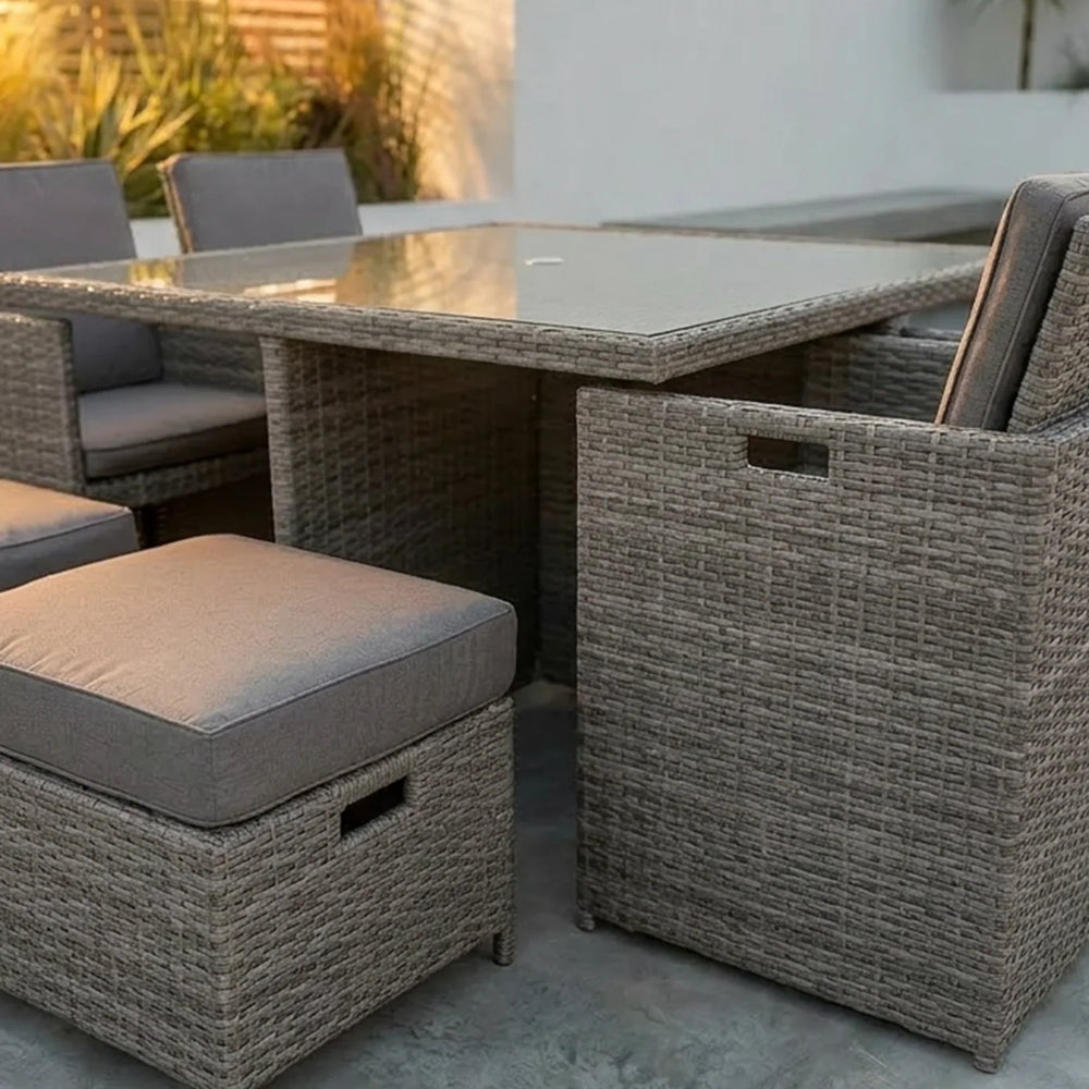 Rattan outdoor dining set with glass table and grey cushioned chairs on patio