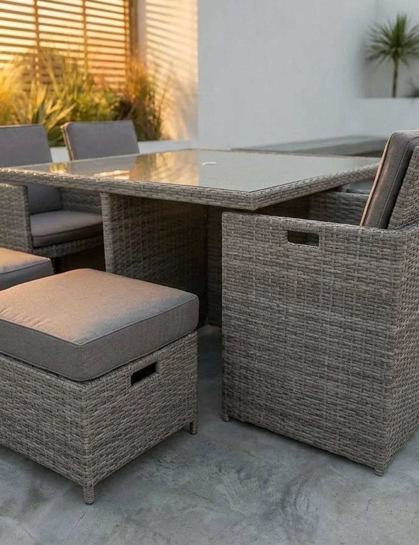Rattan outdoor dining set with glass table and grey cushioned chairs on patio