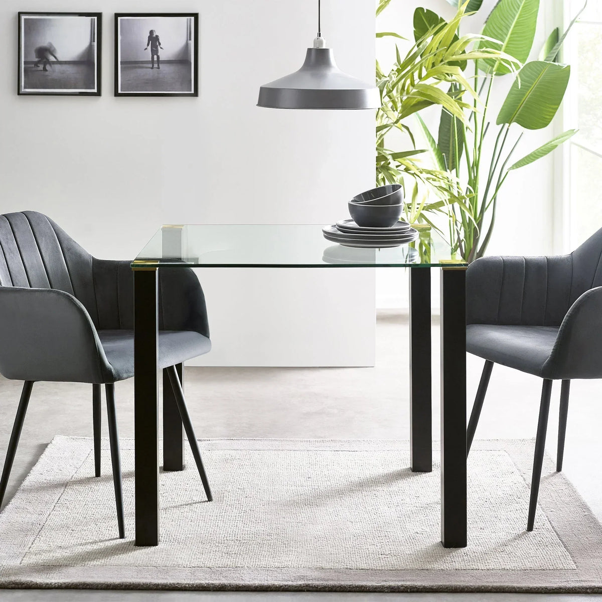 Glass square dining table with black legs and grey chairs in modern room setting
