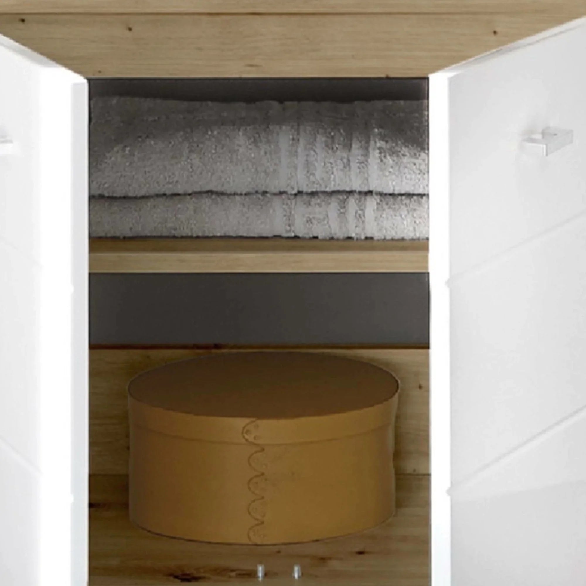 Open storage cabinet with white doors, folded towels and a round storage box on wood shelf