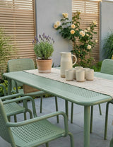 Olive green outdoor dining set with slatted chairs and table on patio, ceramic jug and cups