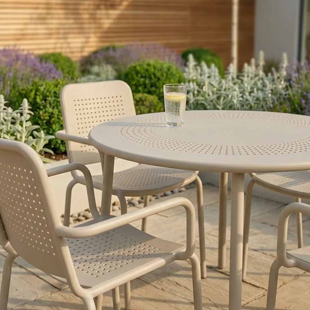 Beige outdoor patio dining set with perforated chairs and round table on stone tiles