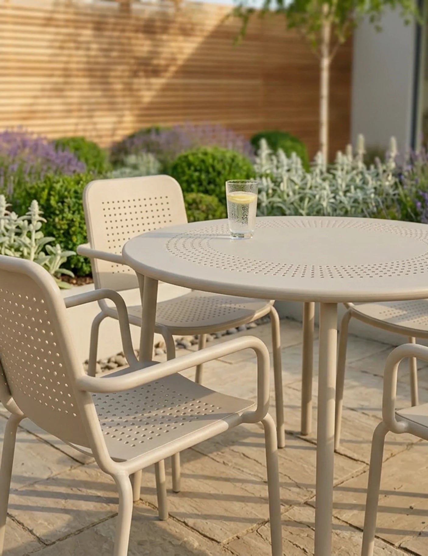 Beige outdoor patio dining set with perforated chairs and round table on stone tiles