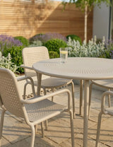 Beige outdoor patio dining set with perforated chairs and round table on stone tiles