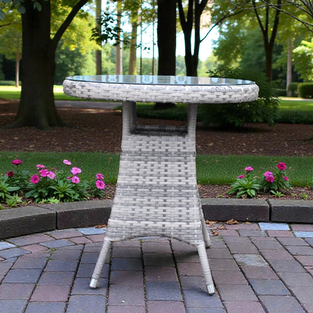 Round rattan garden bistro table with glass top on patio surrounded by flowers