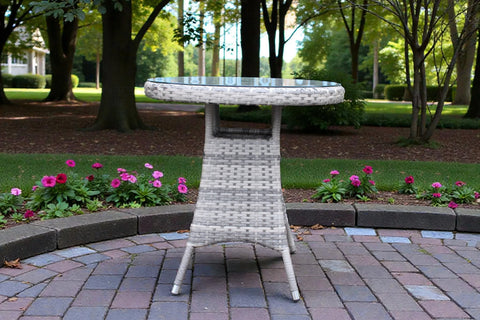 Round rattan garden bistro table with glass top on patio surrounded by flowers