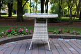 Round rattan garden bistro table with glass top on patio surrounded by flowers