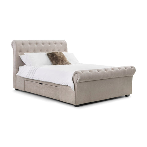 Angled side view of beige fabric button-tufted storage bed with white and brown pillows