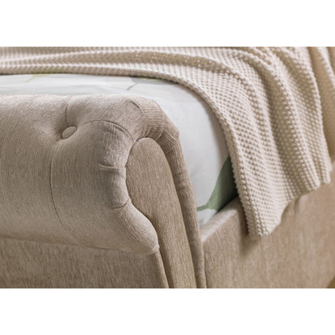 Beige fabric button-tufted rolled armrest with knit blanket draped over bed corner