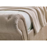 Beige fabric button-tufted rolled armrest with knit blanket draped over bed corner