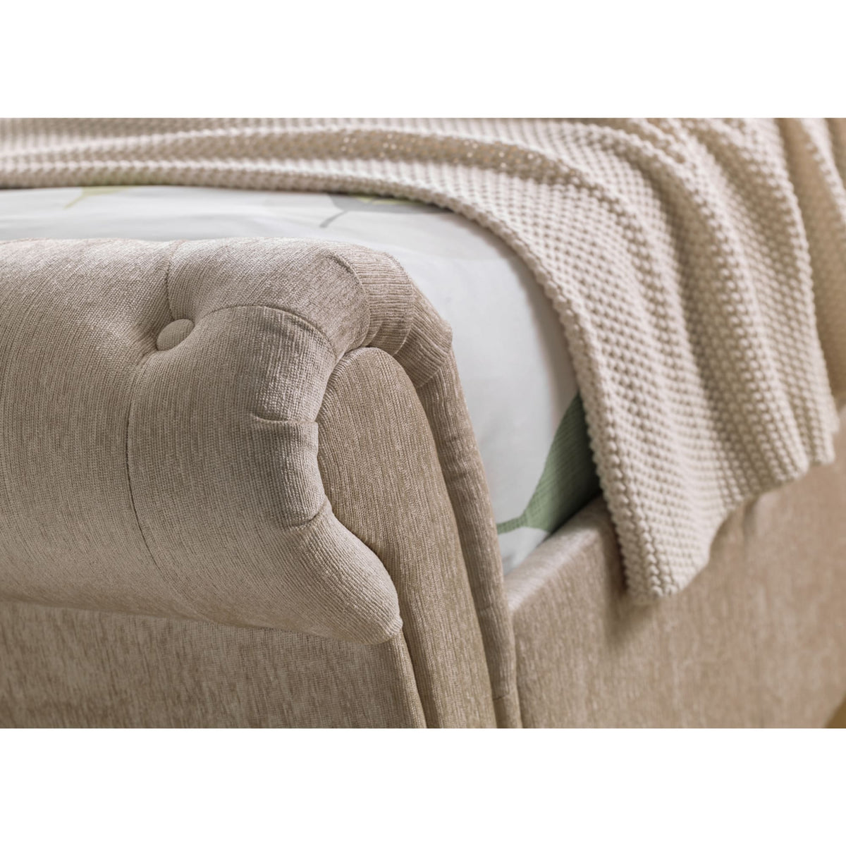 Beige fabric button-tufted rolled armrest with knit blanket draped over bed corner