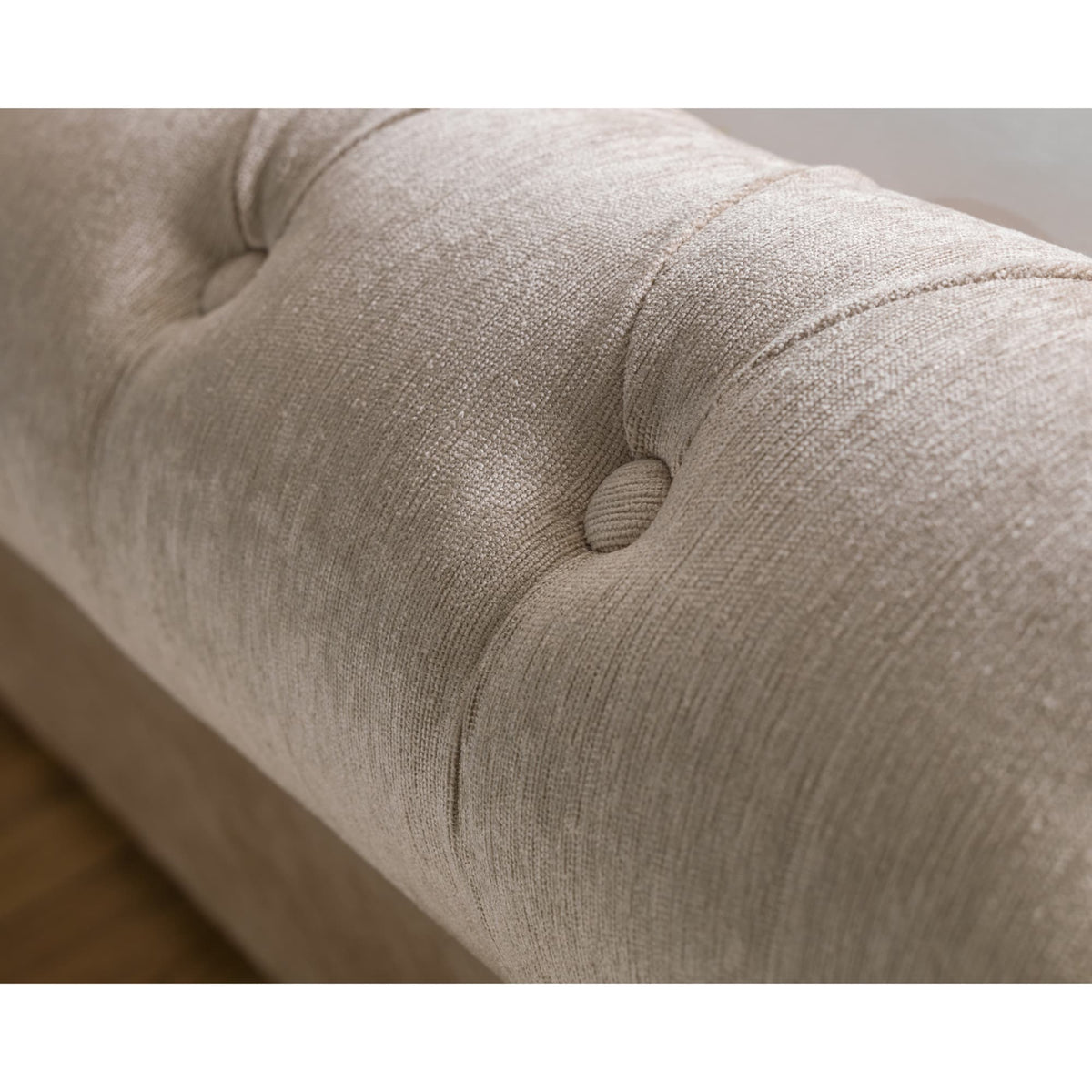 Close-up of beige fabric button tufting on rolled headboard of storage bed