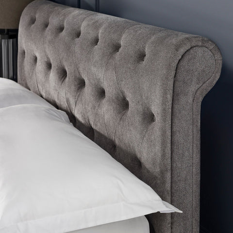 Close-up of grey fabric button-tufted wingback headboard with a white pillow edge visible