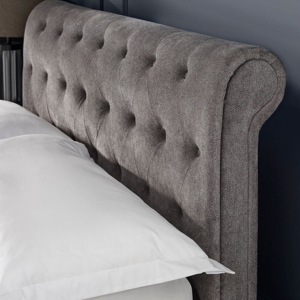 Close-up of grey fabric button-tufted wingback headboard with a white pillow edge visible