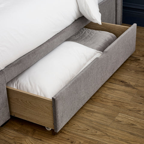 Grey fabric storage drawer open under bed with white bedding inside on wooden floor