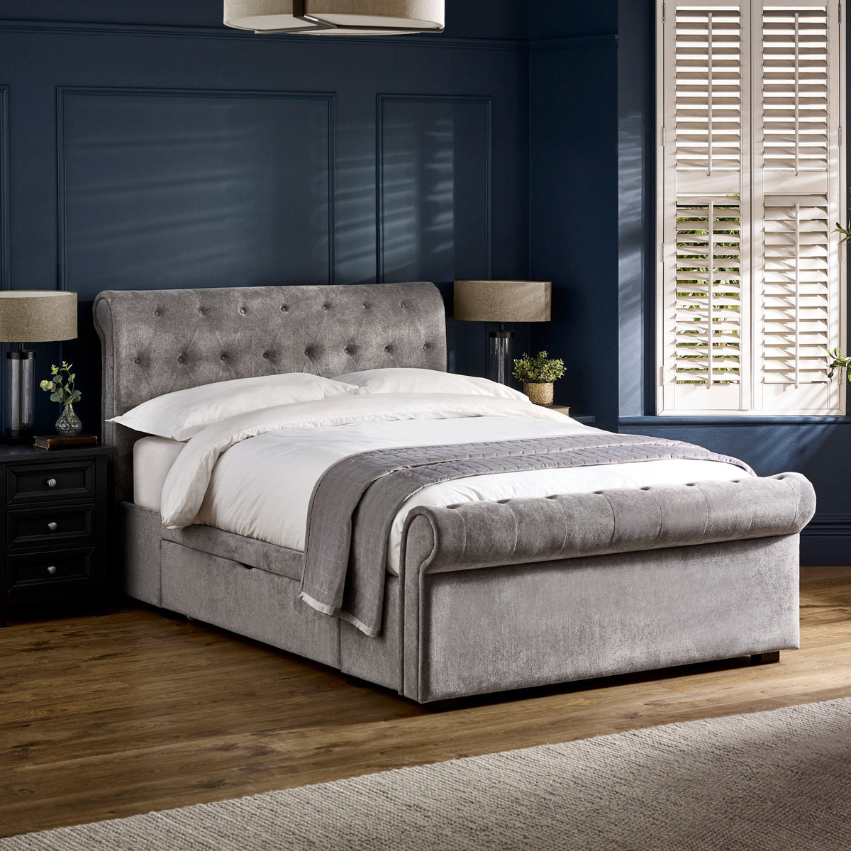 Upholstered grey fabric double bed with tufted headboard and footboard in a dark blue room.
