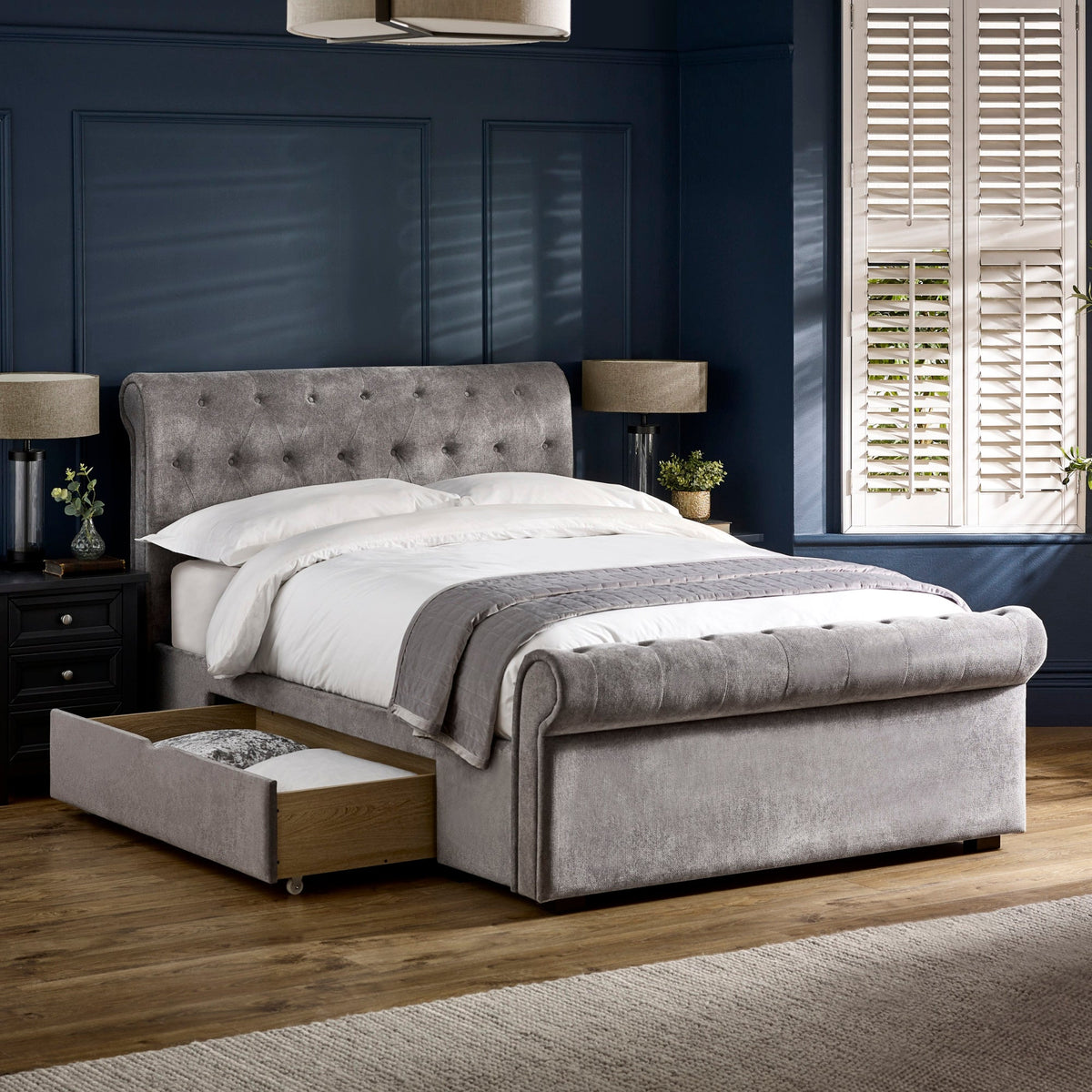 Same grey fabric double bed with left side drawer opened, showing storage space in a dark blue room.