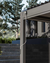 Grey metal pergola corner with manual winding handle and mesh side panel, outdoor setting