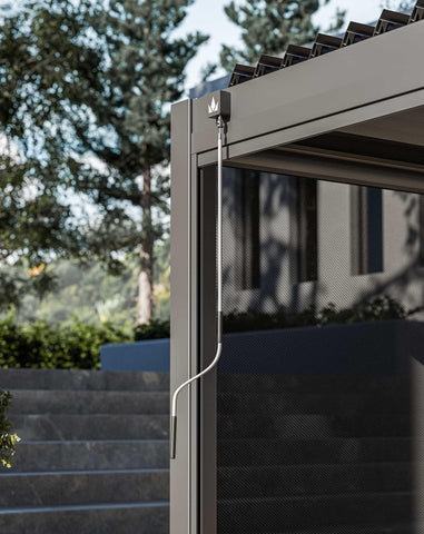 Grey aluminium pergola corner with manual winding handle and mesh privacy screen outdoors