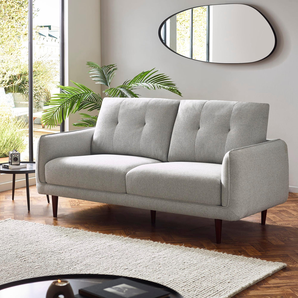 Light grey fabric sofa with tufted cushions in modern living room with wooden flooring