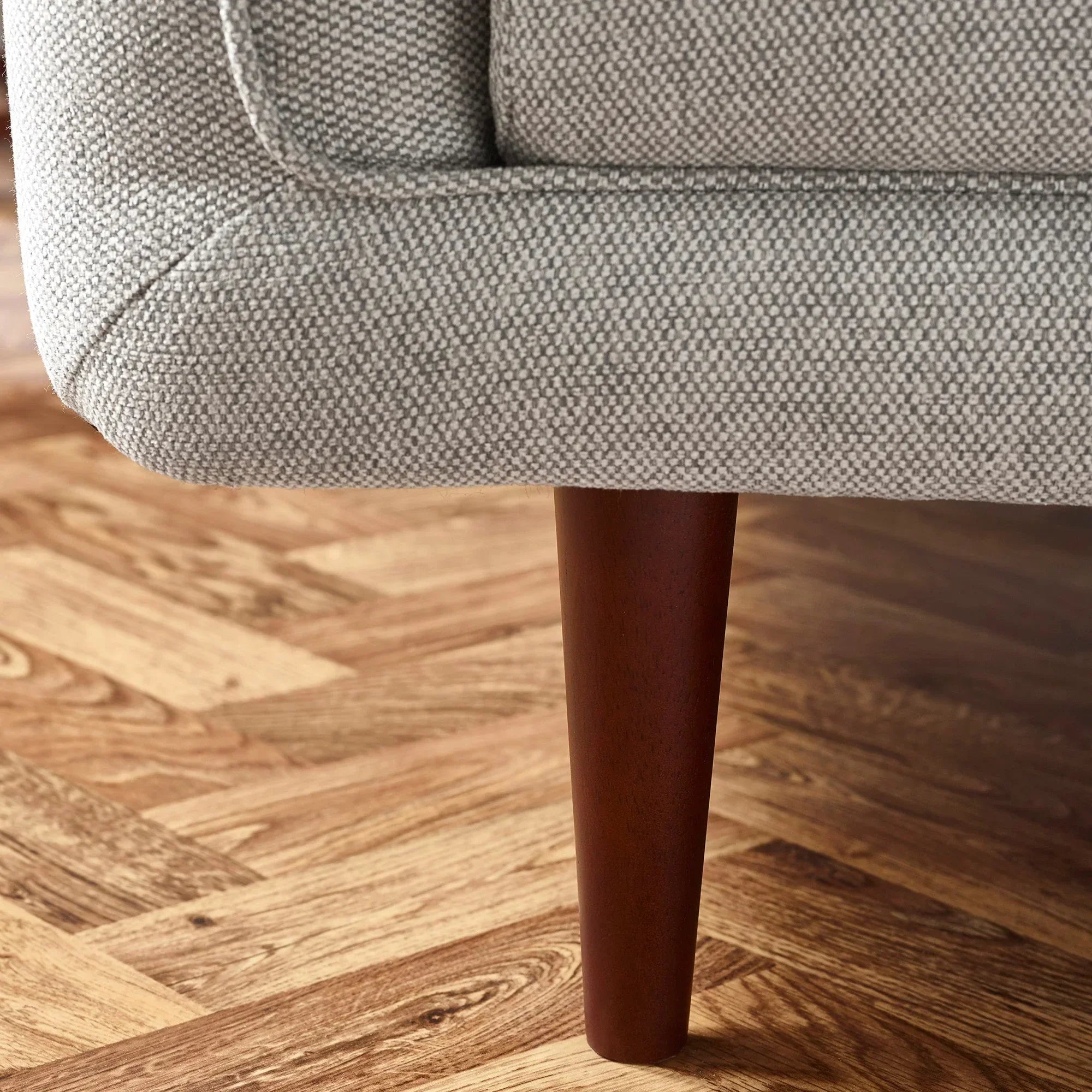 Grey fabric sofa corner with wooden leg on parquet floor