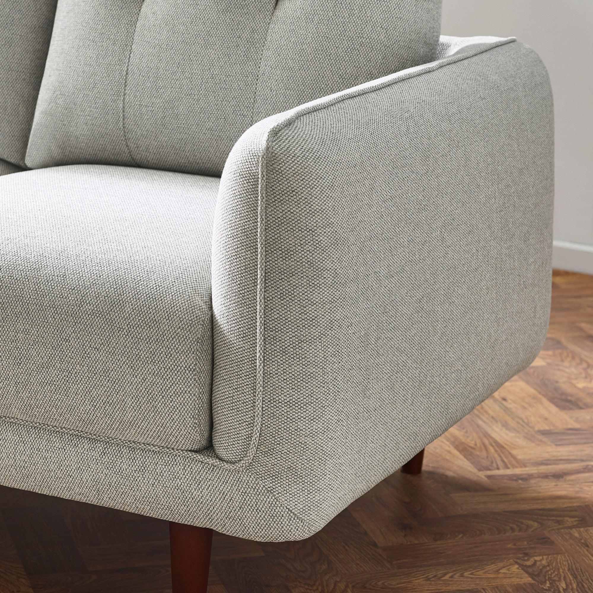 Light grey fabric sofa arm detail with wooden legs on herringbone floor