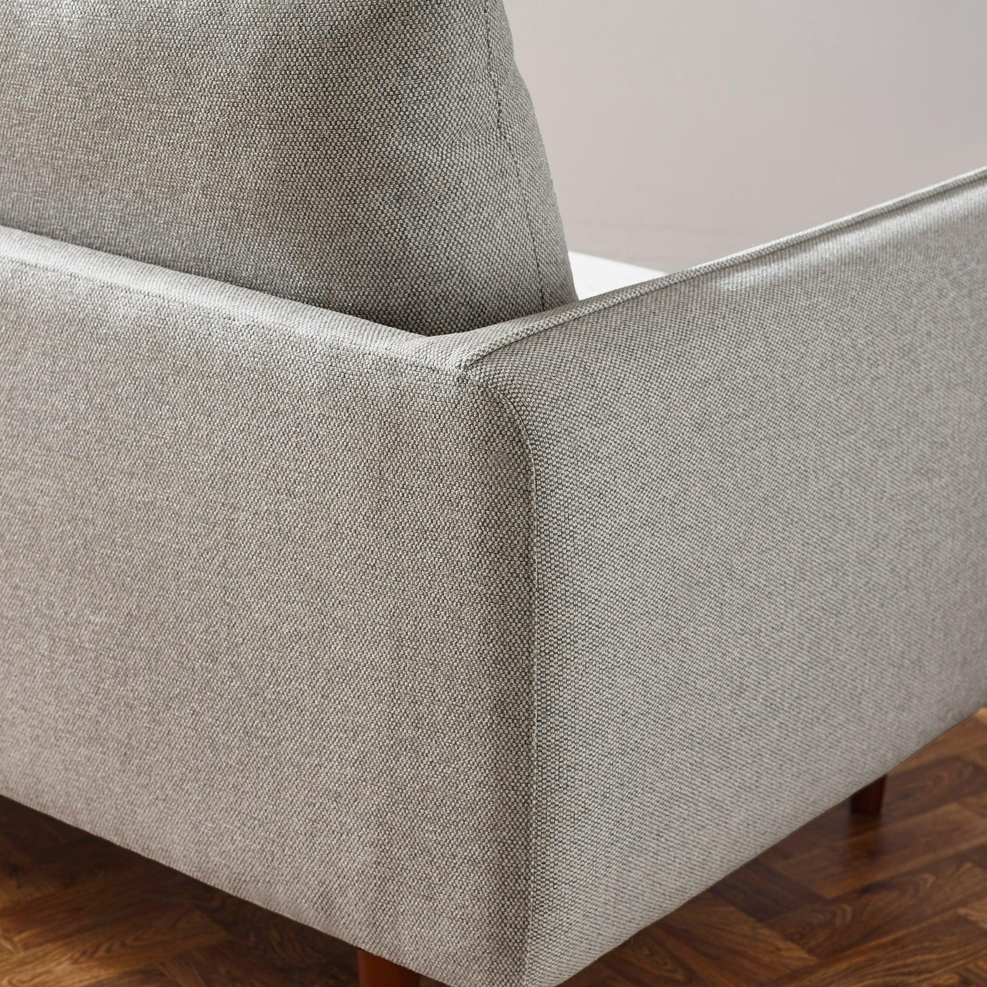 Close-up of grey fabric sofa arm and cushion with wooden floor background