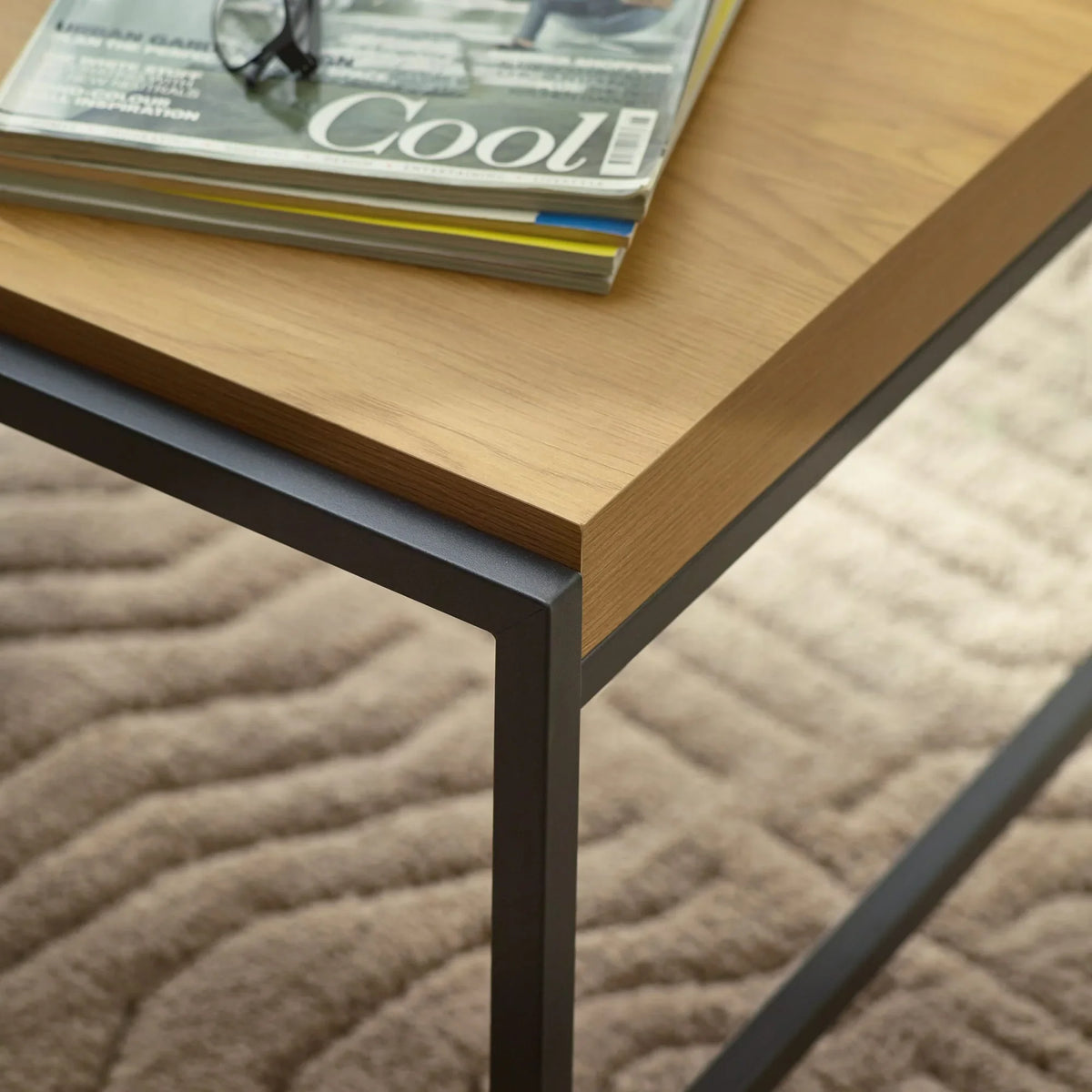 Wood and metal coffee table with magazines on top, close view of corner and legs