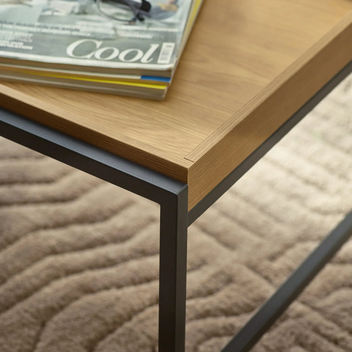 Oak effect coffee table with black metal legs, close up corner detail on textured rug