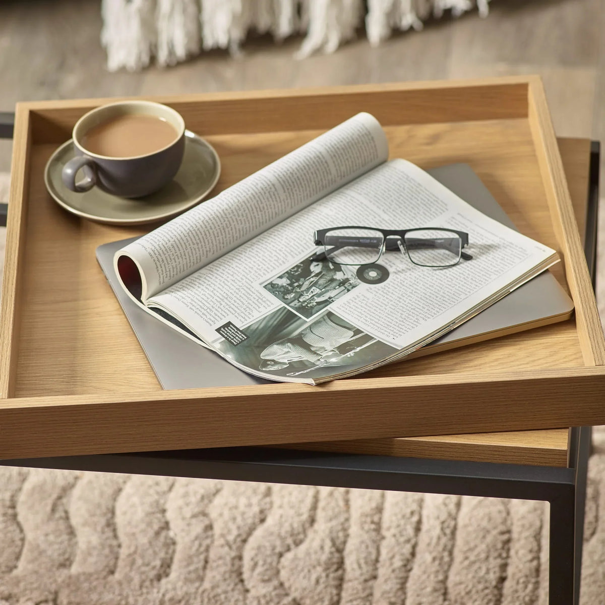 modern wooden side table with open magazine, glasses, and coffee cup on neutral rug