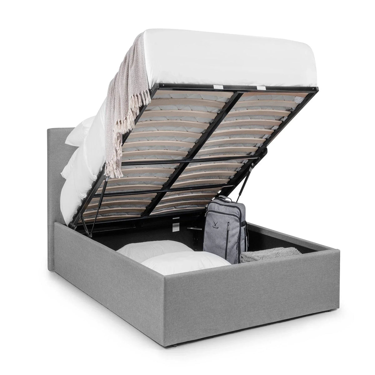 Grey upholstered lift-up storage bed with open ottoman base, pillows and luggage inside