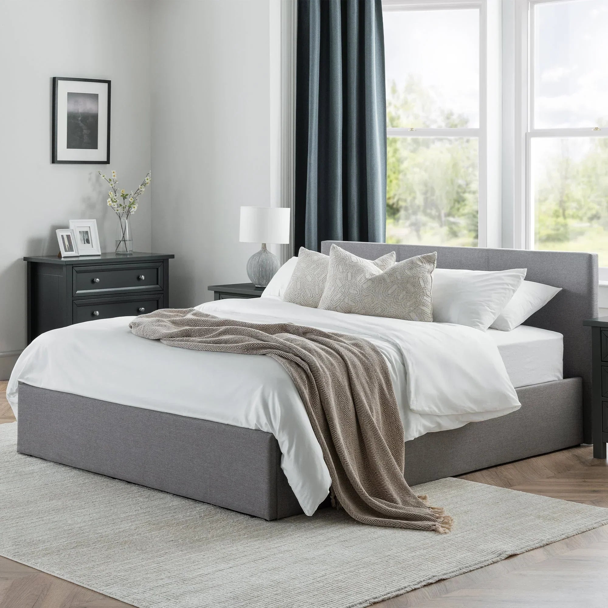 Grey lift-up storage bed with headboard in modern bedroom, white bedding and beige throw blanket