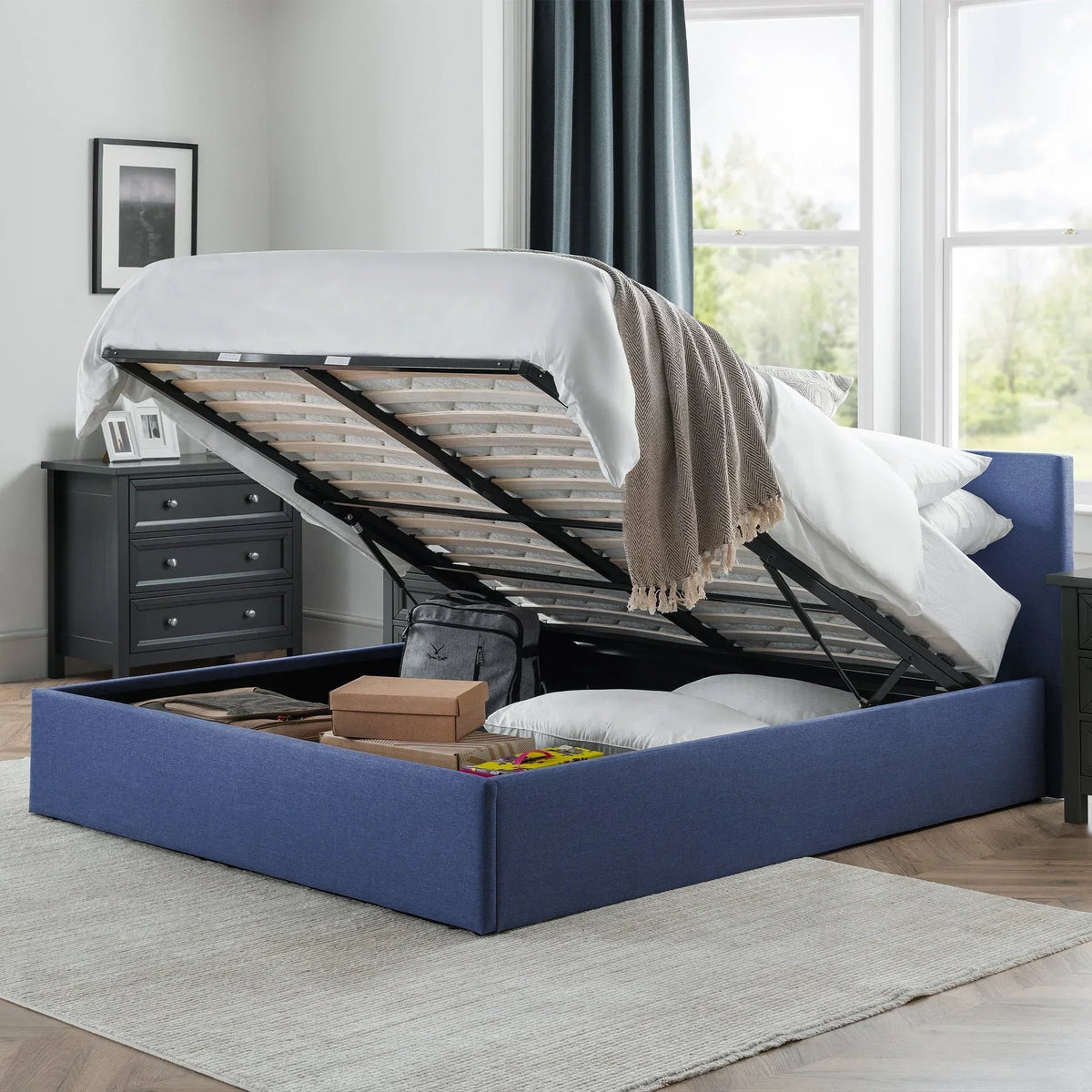 blue lift-up storage bed with open base showing pillows and boxes in modern bedroom