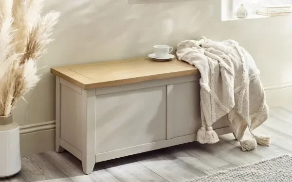 Cream storage bench with oak top, throw, and cup in bright living room setting