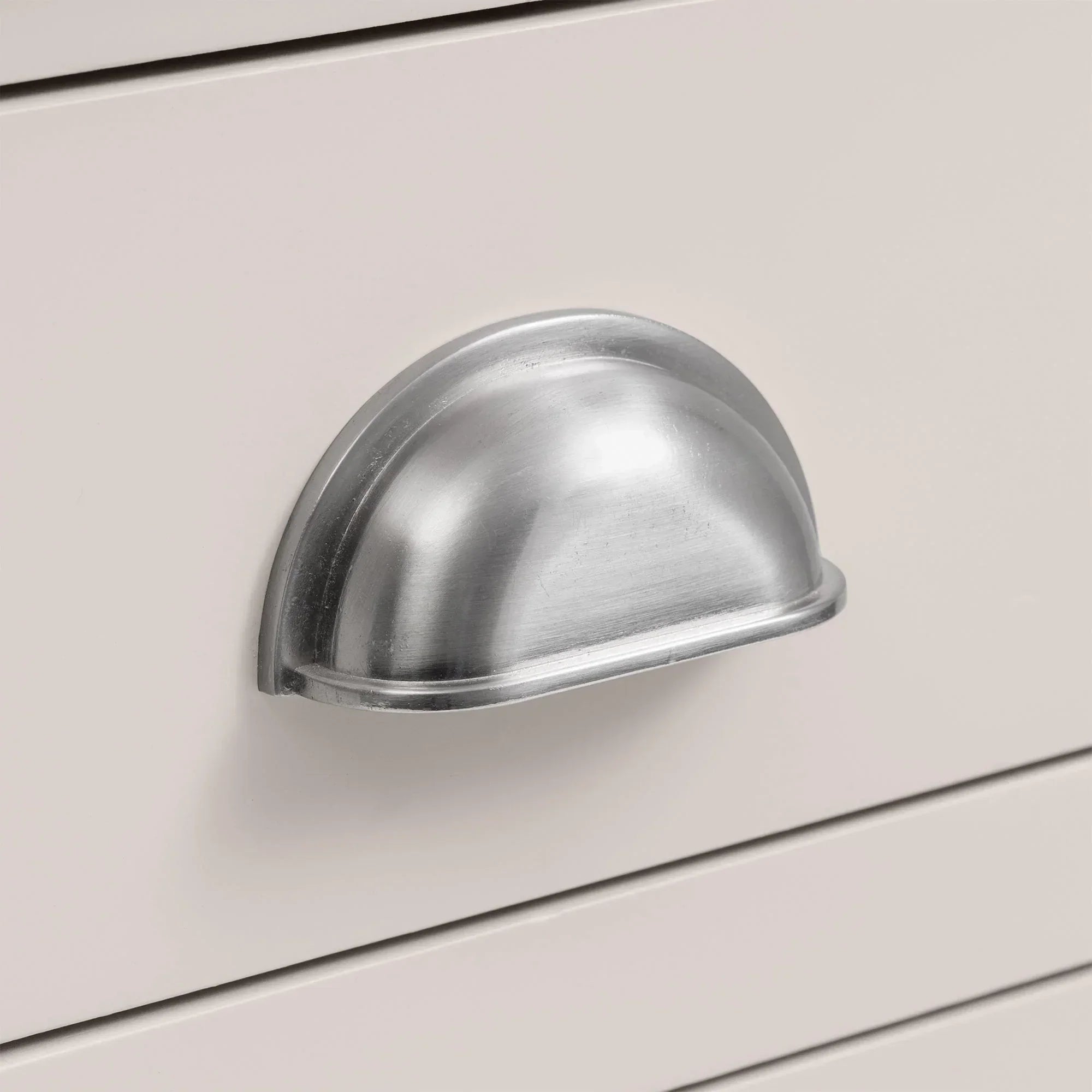 Silver cup handle on white wooden bedside table drawer close-up