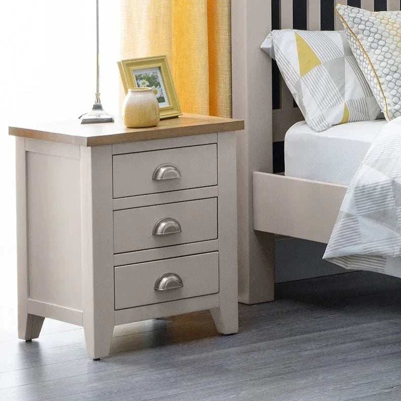 Cream bedside table with three drawers and silver handles beside a bed in a modern bedroom