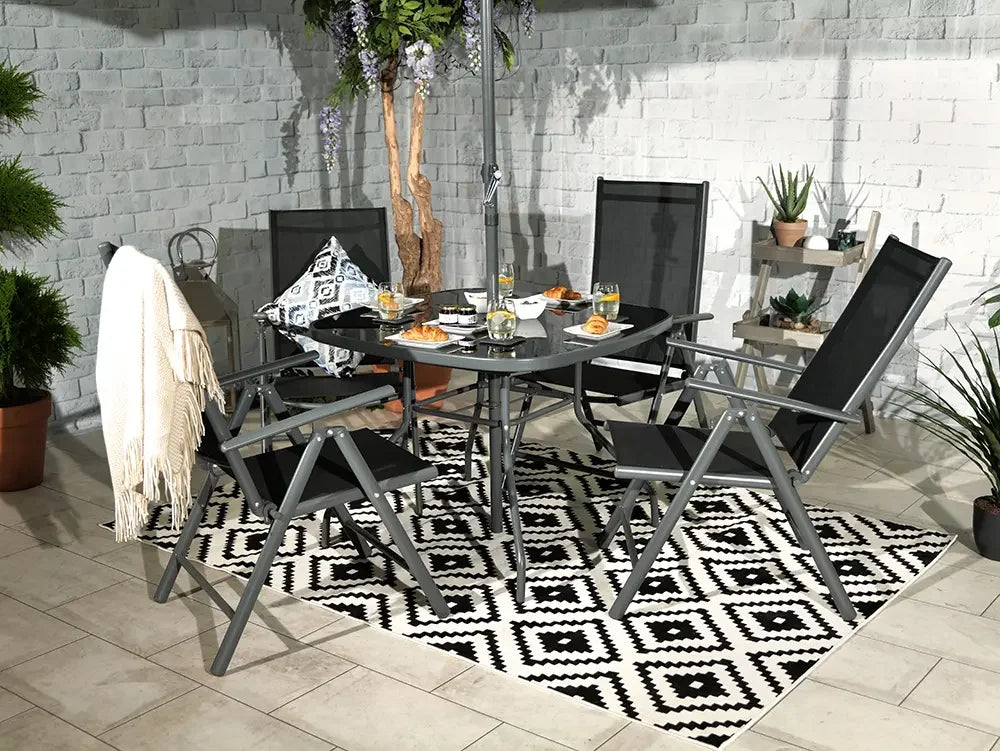 Black and grey outdoor dining set with glass table and four mesh chairs on patio rug