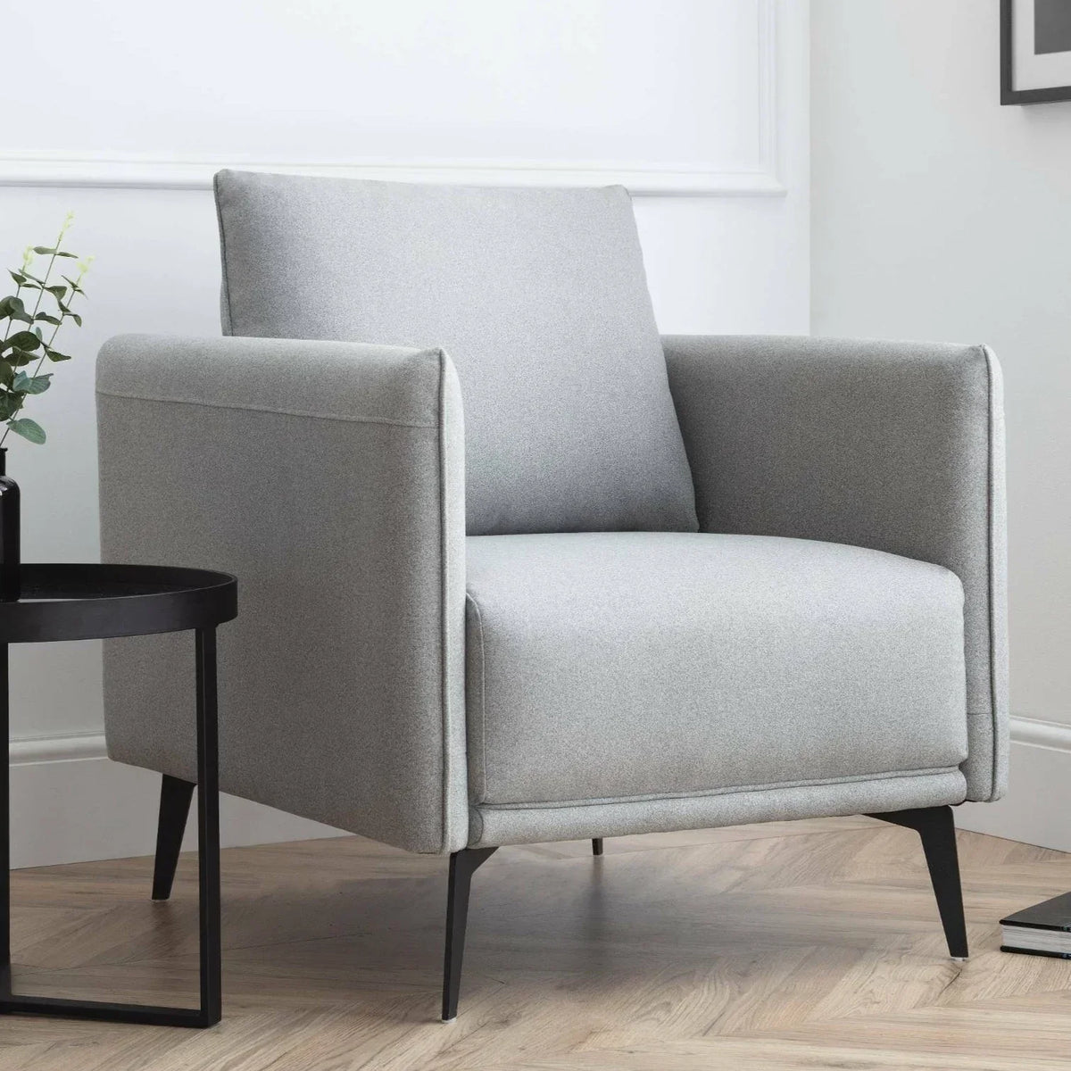 Modern grey fabric armchair with black legs beside round side table on wooden floor