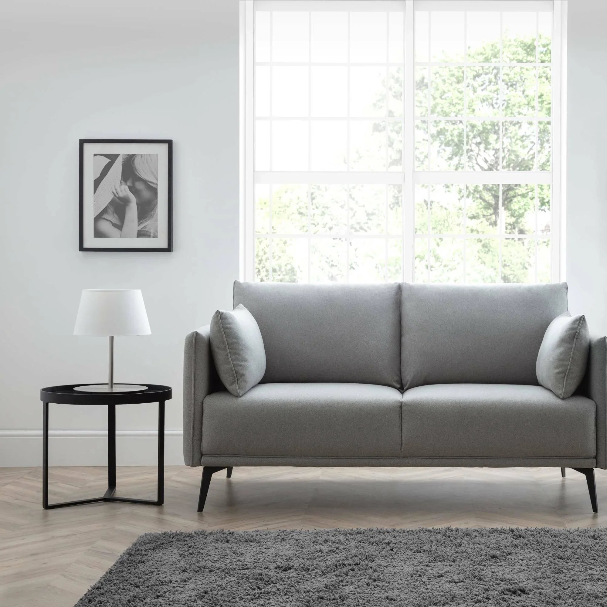 Grey fabric 2 seater sofa with slim arms in modern living room beside round black side table