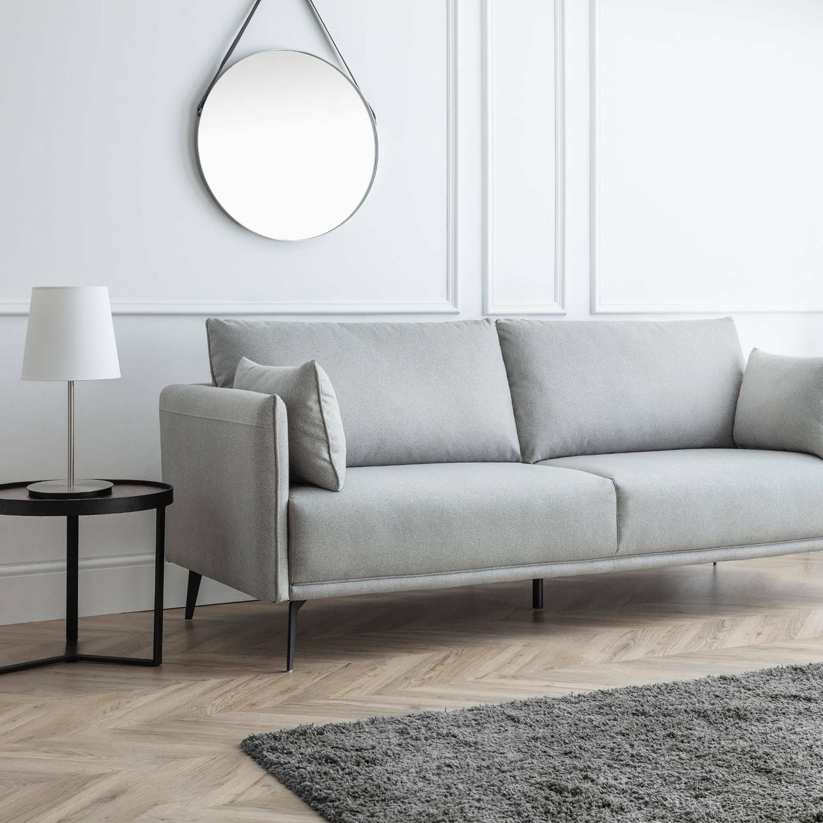 Light grey 3 seater sofa with slim legs in modern living room, beside round black side table