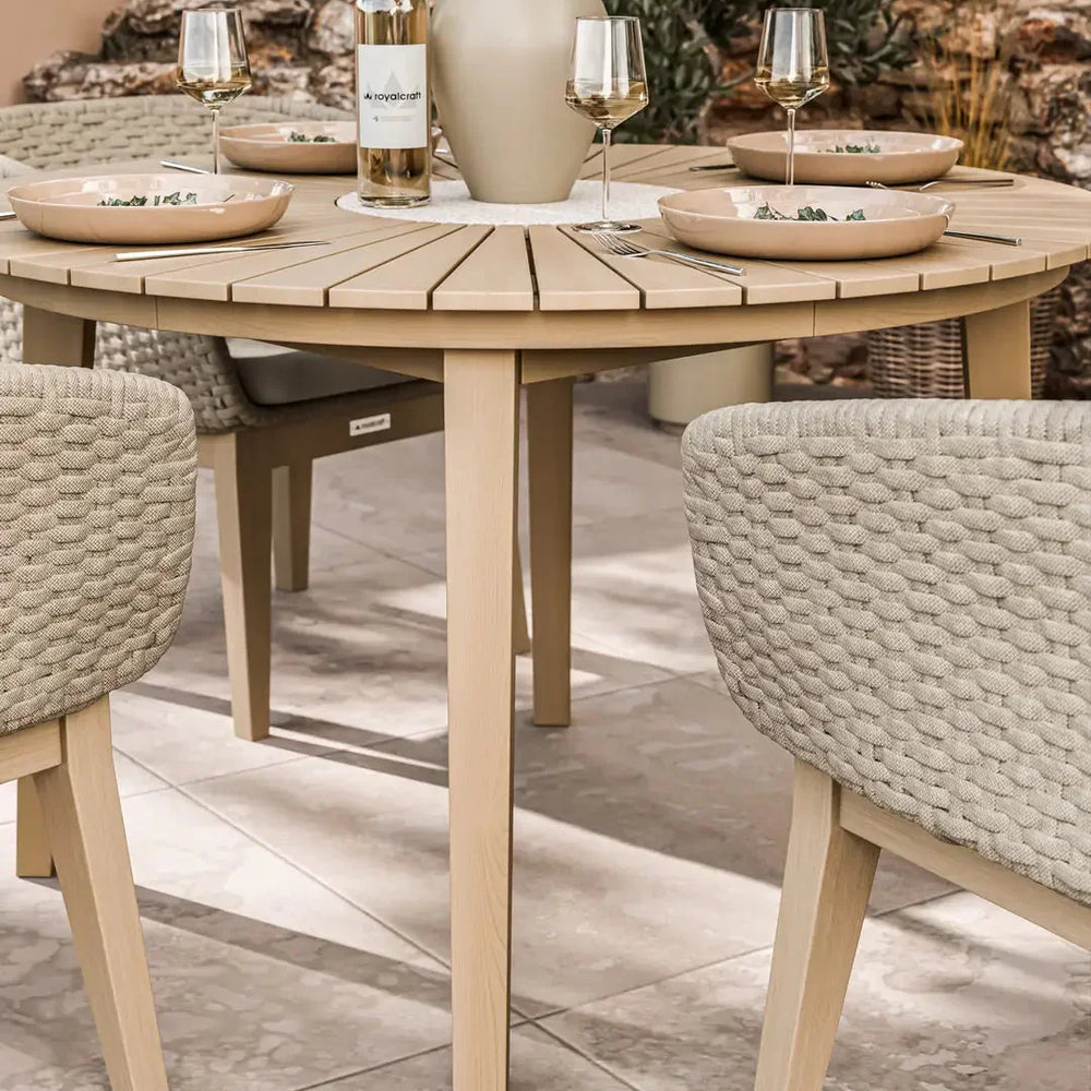 Round wood outdoor dining table with rope chairs set for four on patio tiles