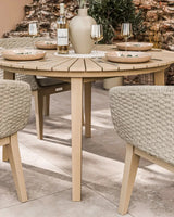 Round wood outdoor dining table with rope chairs set for four on patio tiles