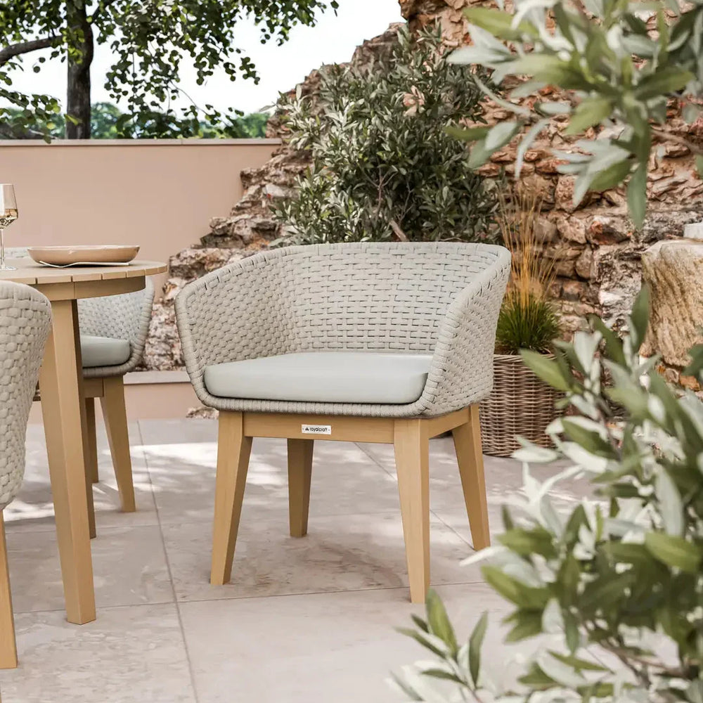 Outdoor rattan dining chair with light cushion and wooden legs on tiled patio